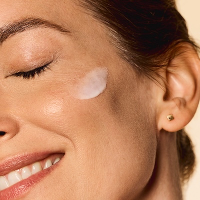 Mujer sonriendo con crema hidratante facial aplicada sobre la mejilla.