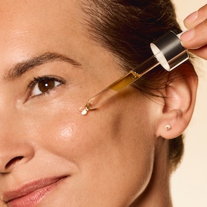 Aplicación del Sleeping Oil Excellageᴺᵀ de Institut Esthederm en el rostro de una mujer madura; textura oleosa dorada que nutre intensamente la piel durante la noche.